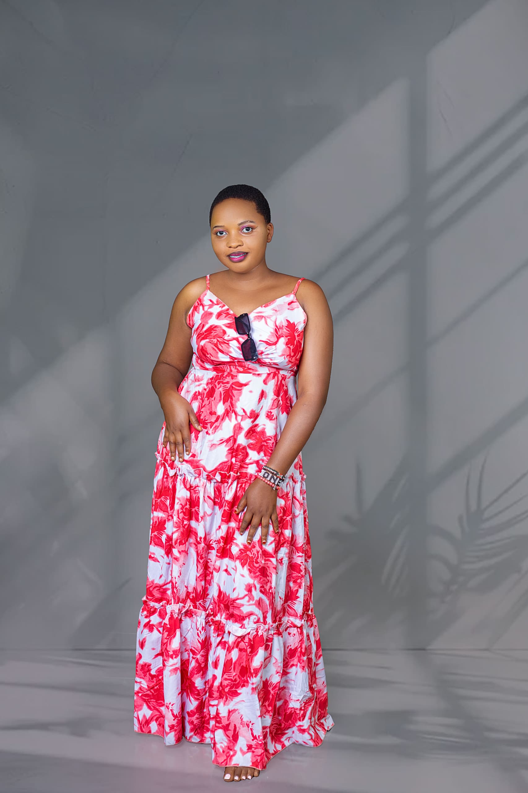 Person standing in a long red-and-white floral dress against a gray studio backdrop